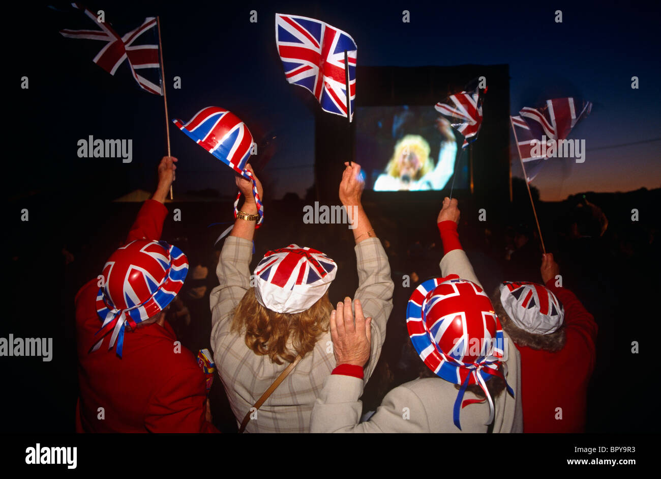 Quatre femmes sont vus de dos portant des chapeaux Union Jack et agitaient des drapeaux drapeau national de la Grande-Bretagne. Banque D'Images
