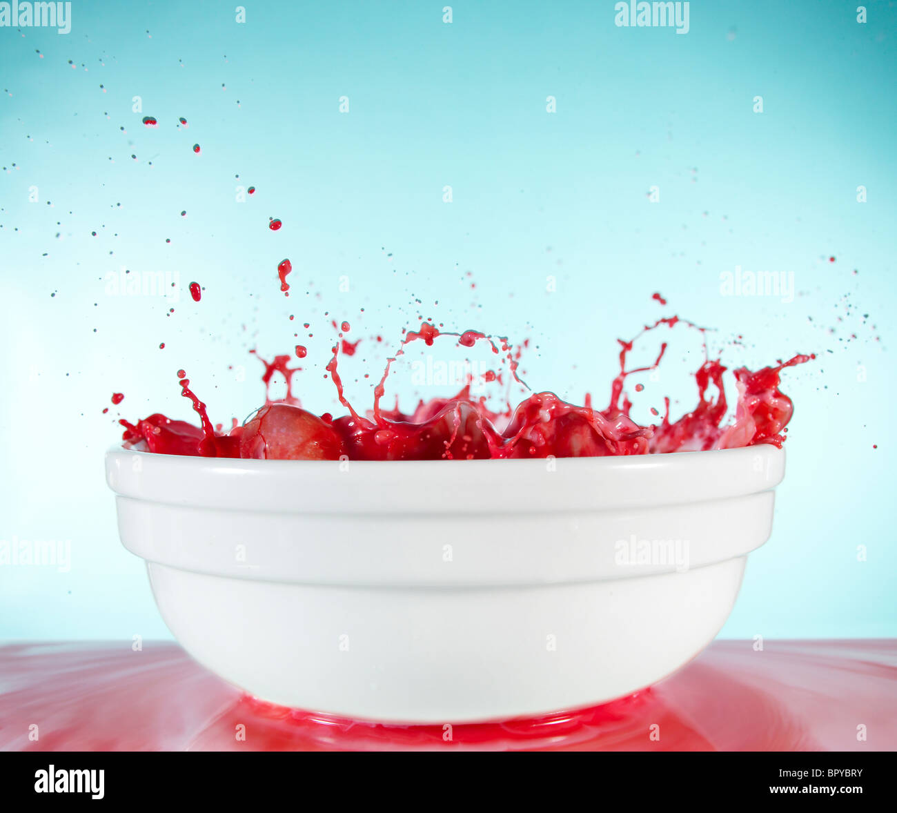 Des bulles et des éclaboussures de liquide rouge dans un bol blanc Banque D'Images