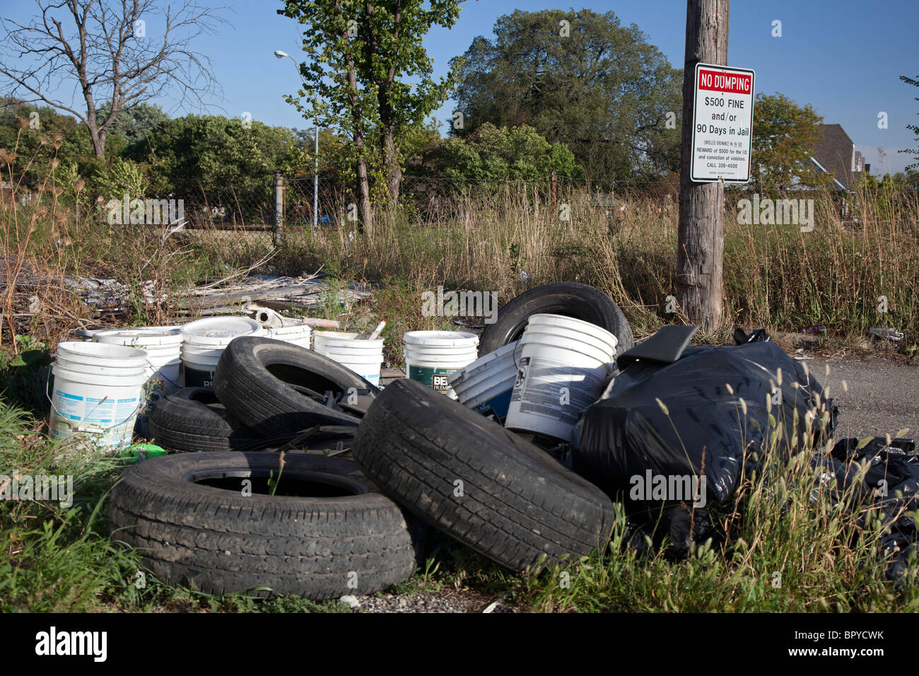 Detroit, Michigan - les vieux pneus et autres déchets sont déversés dans une ruelle à côté d'un signe d'avertissement des pénalités pour dépôt illégal. Banque D'Images