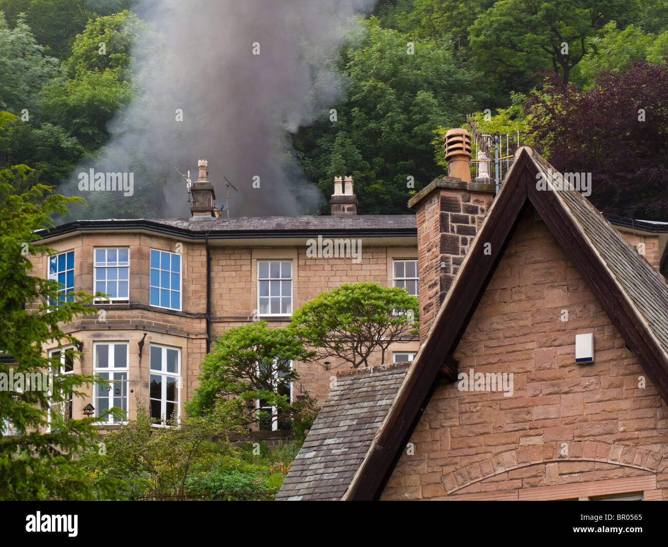 Feu à la maison avec de la fumée noire s'échapper de la toiture et arbres en arrière-plan Banque D'Images