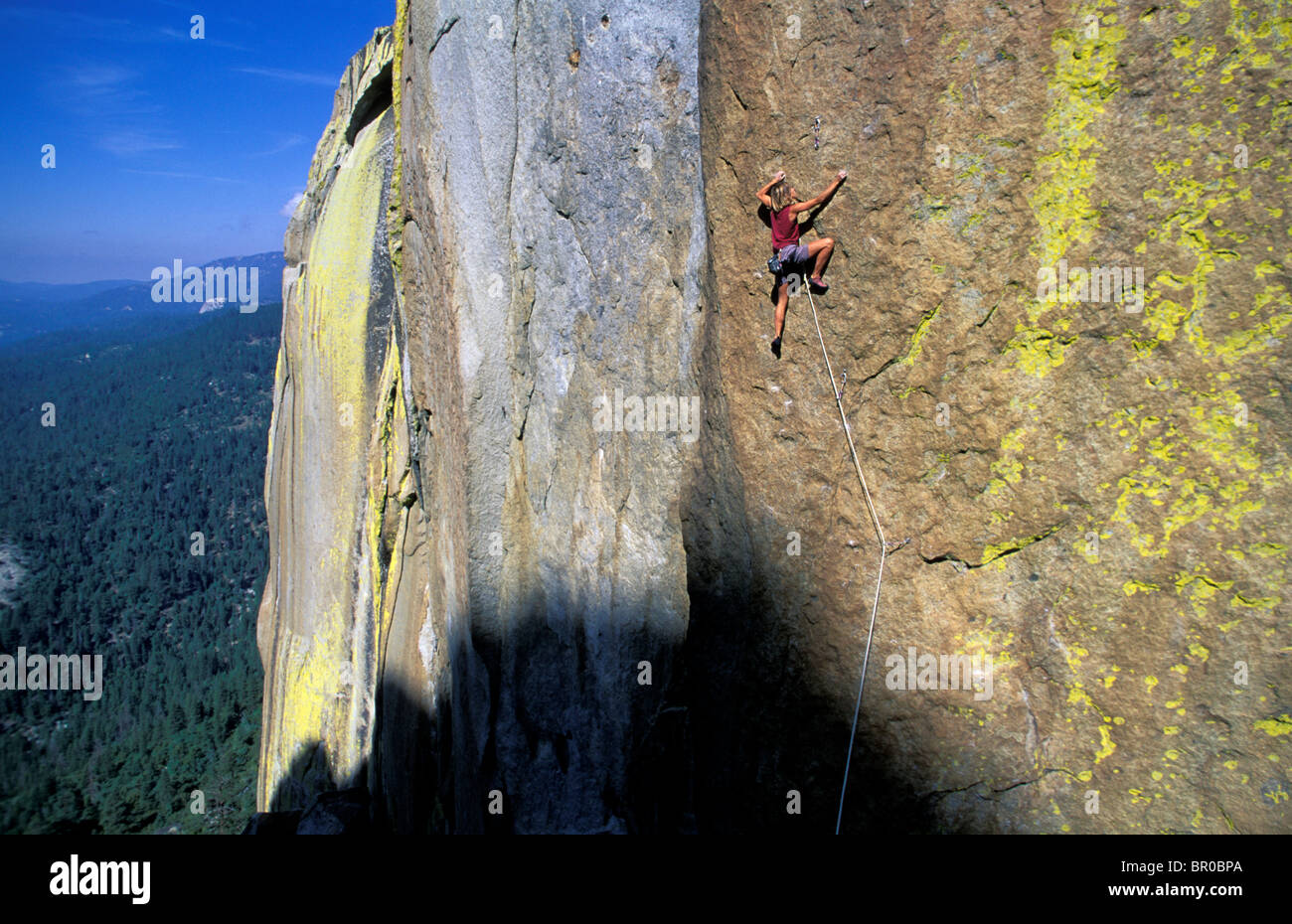 Un female rock climber sertissage d'une attente sur une falaise au-dessus d'une forêt. Banque D'Images