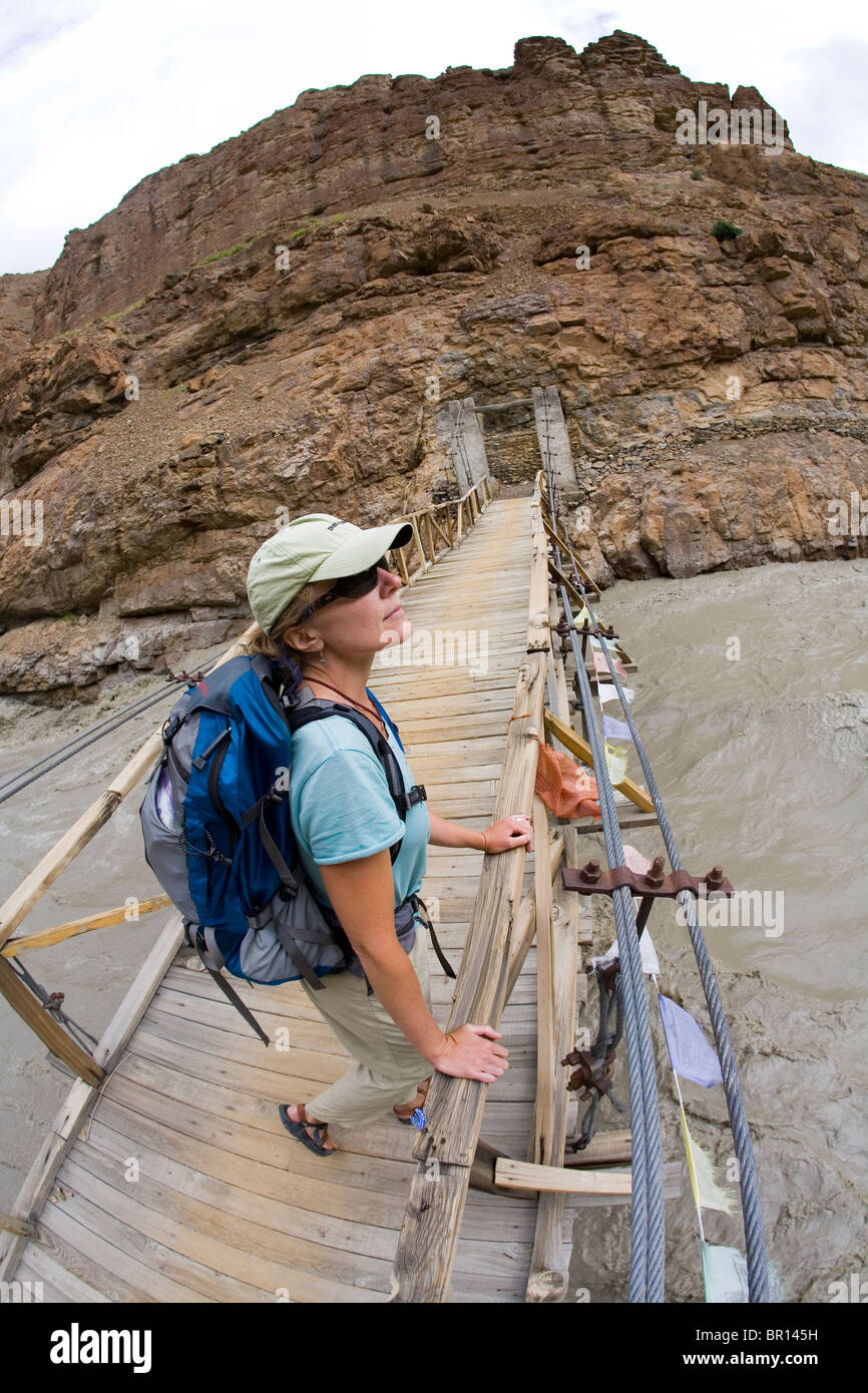 Femme avec sac à dos est sur pont de bois sur la rivière à proximité de monastère de Phuktal, dans des montagnes de haute altitude au Zanskar n Banque D'Images