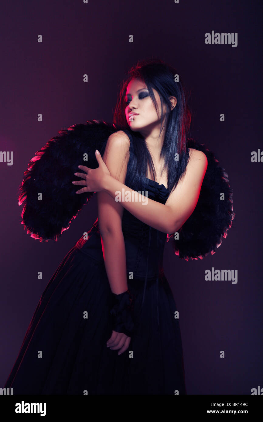 Dame brune avec ailes noires sur un fond sombre. Lumière colorée ajouté par le filtre d'éclairage en studio Banque D'Images
