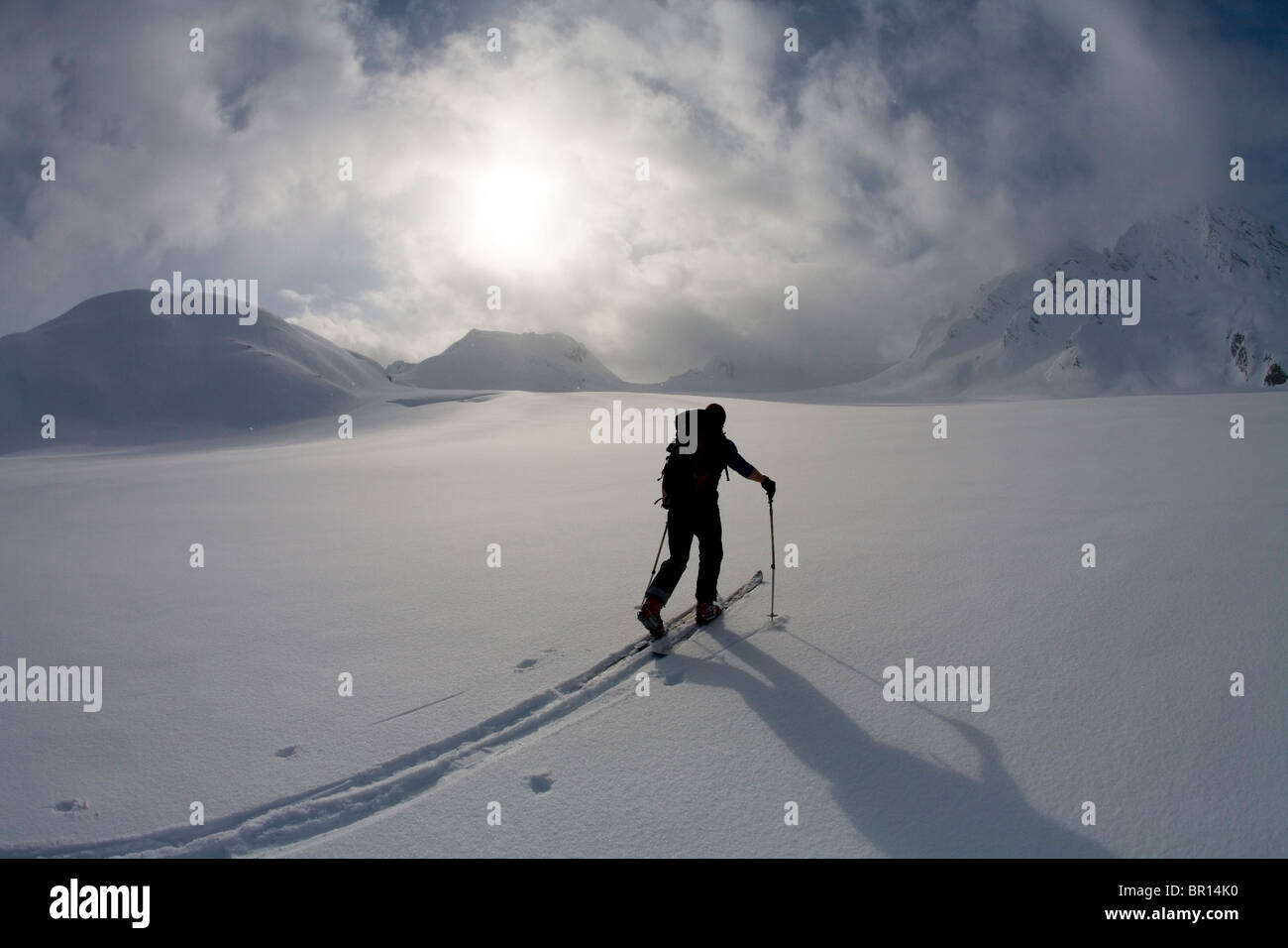 La skieuse de l'arrière-pays traverse sous feu glacier jour ciel d'orage. Banque D'Images