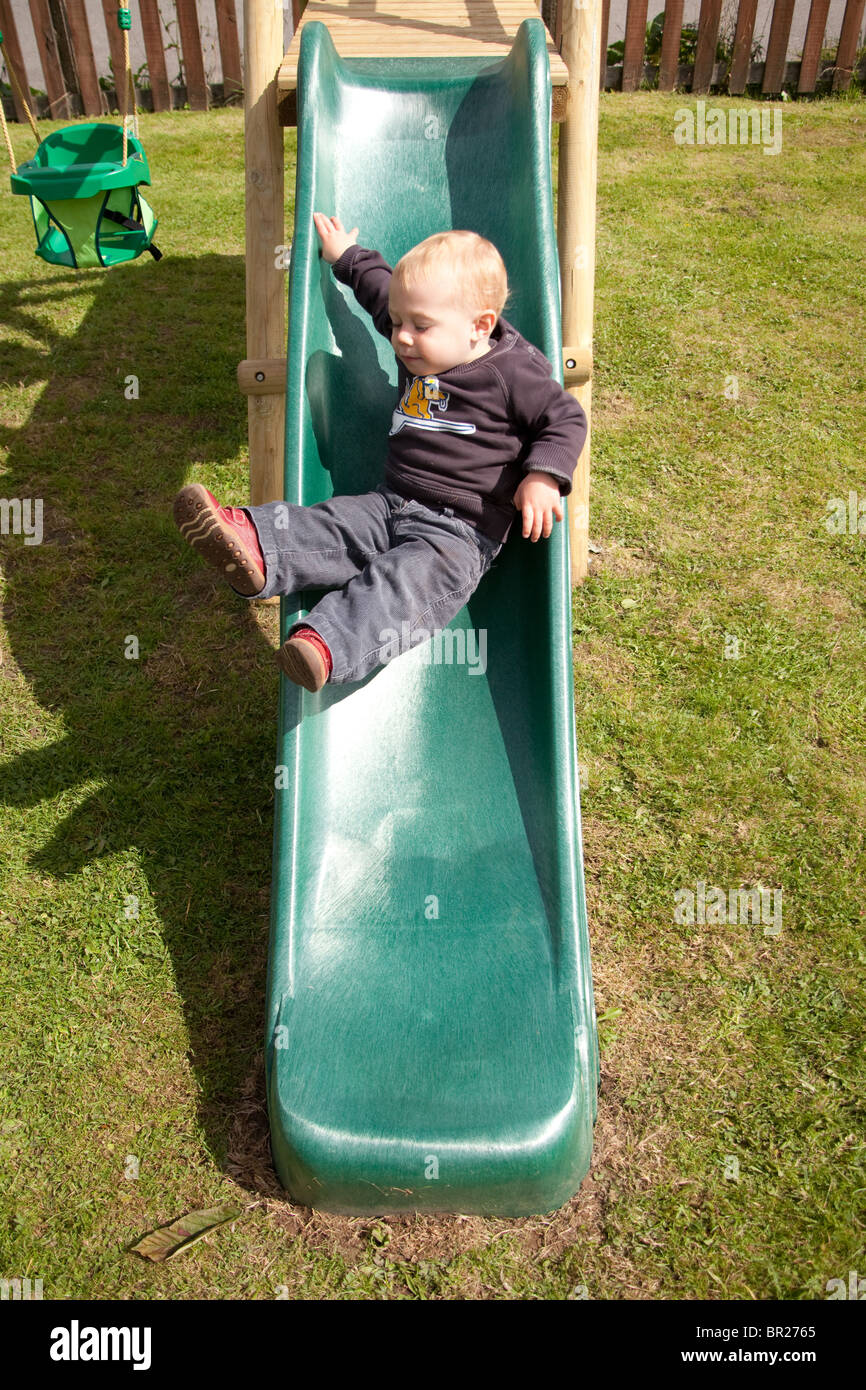 Jeune garçon bambin de 18 mois sur une diapositive, Hampshire, Angleterre, Royaume-Uni. Banque D'Images