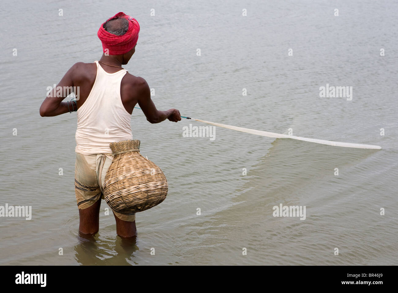 Un pêcheur indien avec un panier de pêche est par net dans la mer près du village de pêche sur la mer de Gopalpur, Orissa, Inde. Banque D'Images
