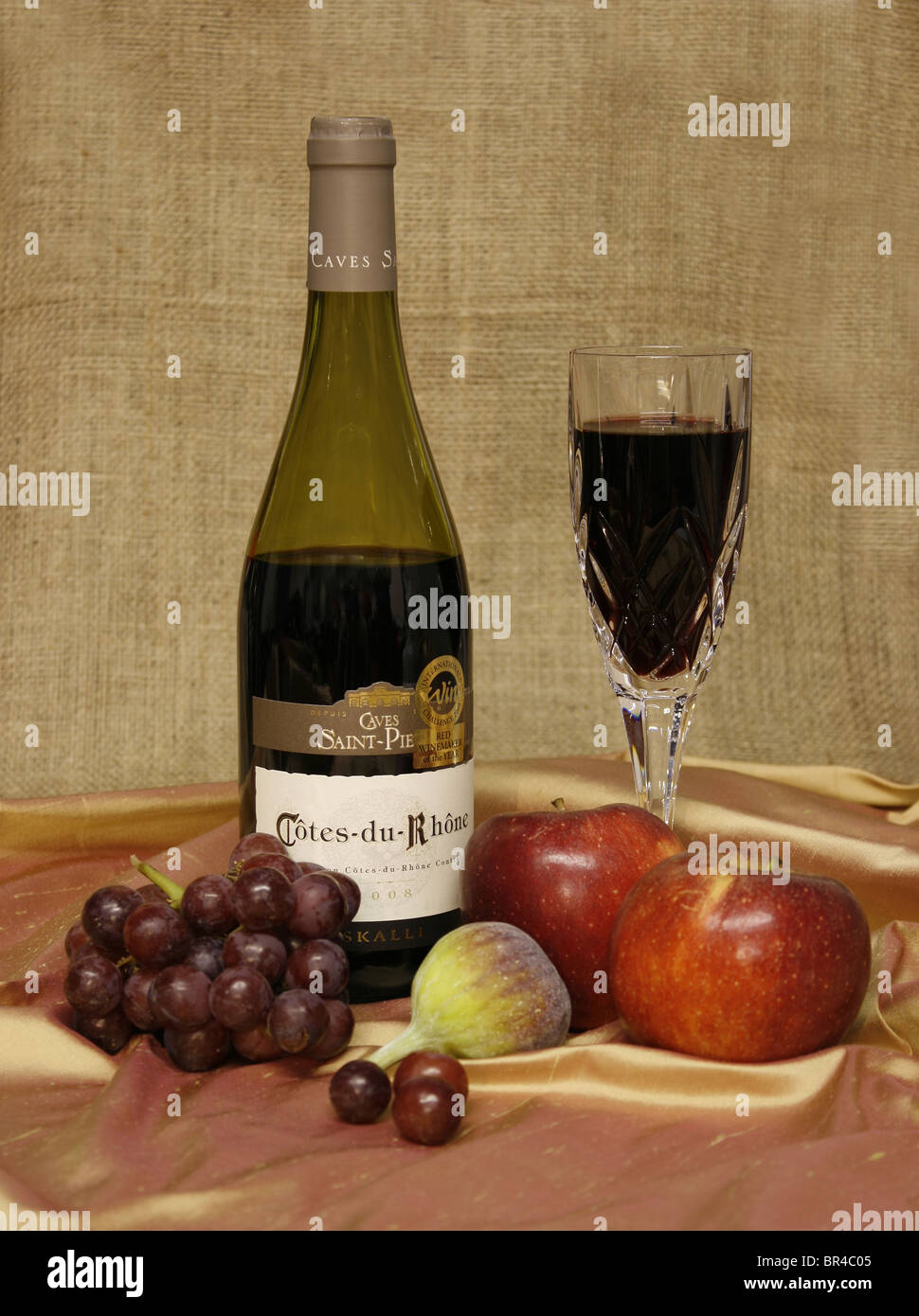 Bouteille de vin rouge et de vin dans un verre, avec des fruits sur un fond de toile. Banque D'Images