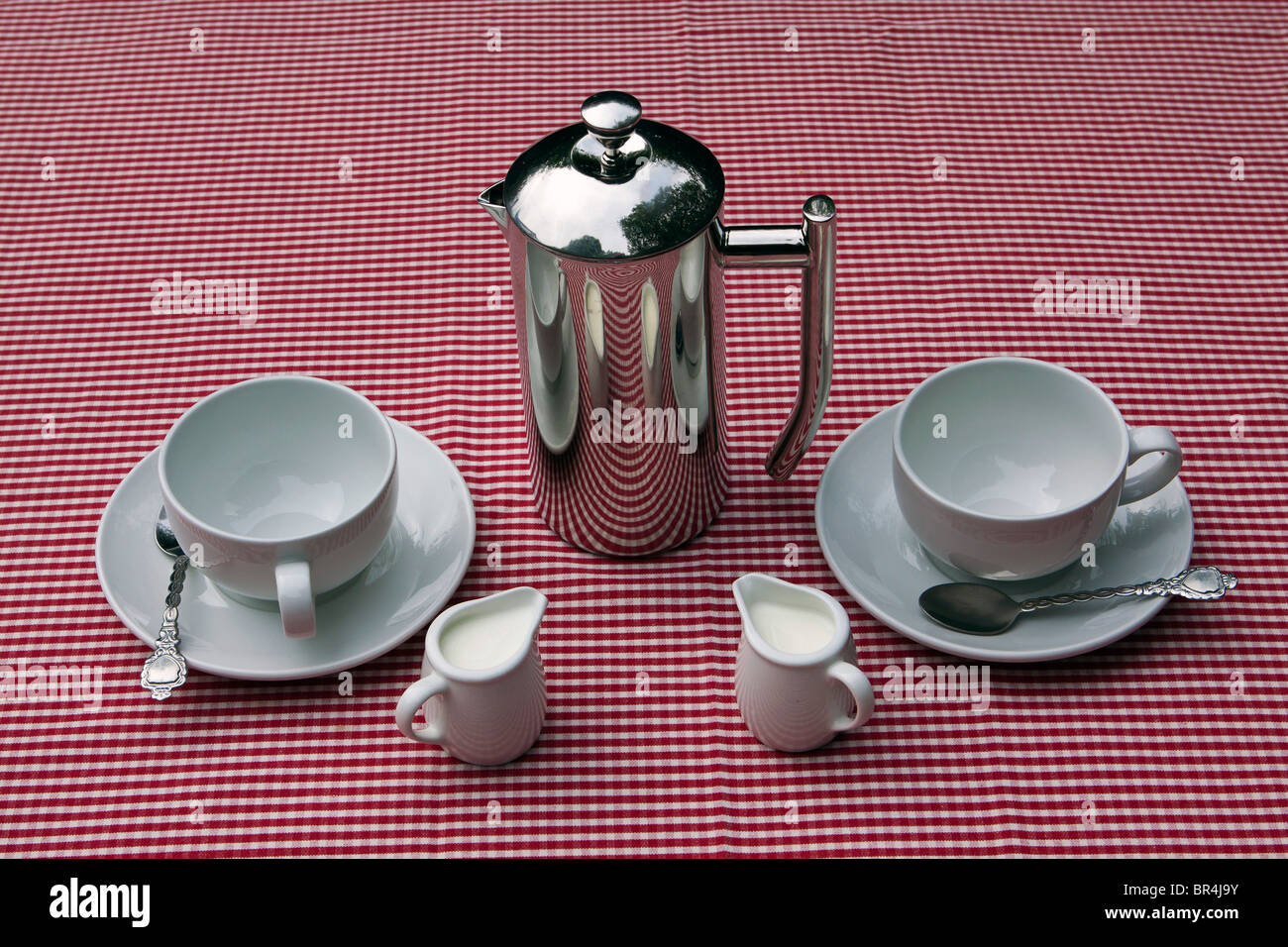 Un pot de café et tasses et soucoupes sur une nappe blanche et rouge Banque D'Images