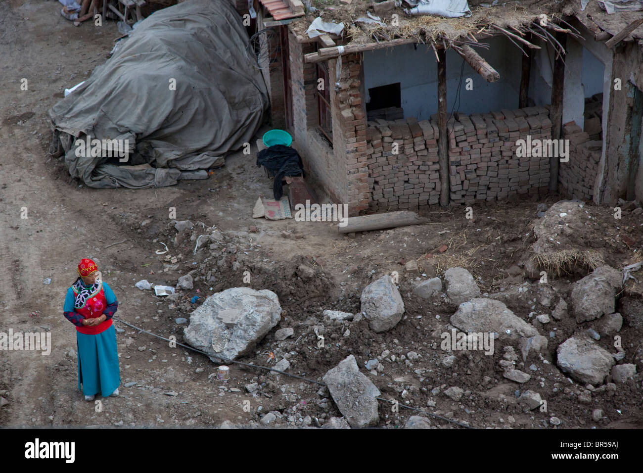 Jeune femme en costume traditionnel tibétain comité permanent par une maison en construction en Chine Gansu Xiahe. Banque D'Images