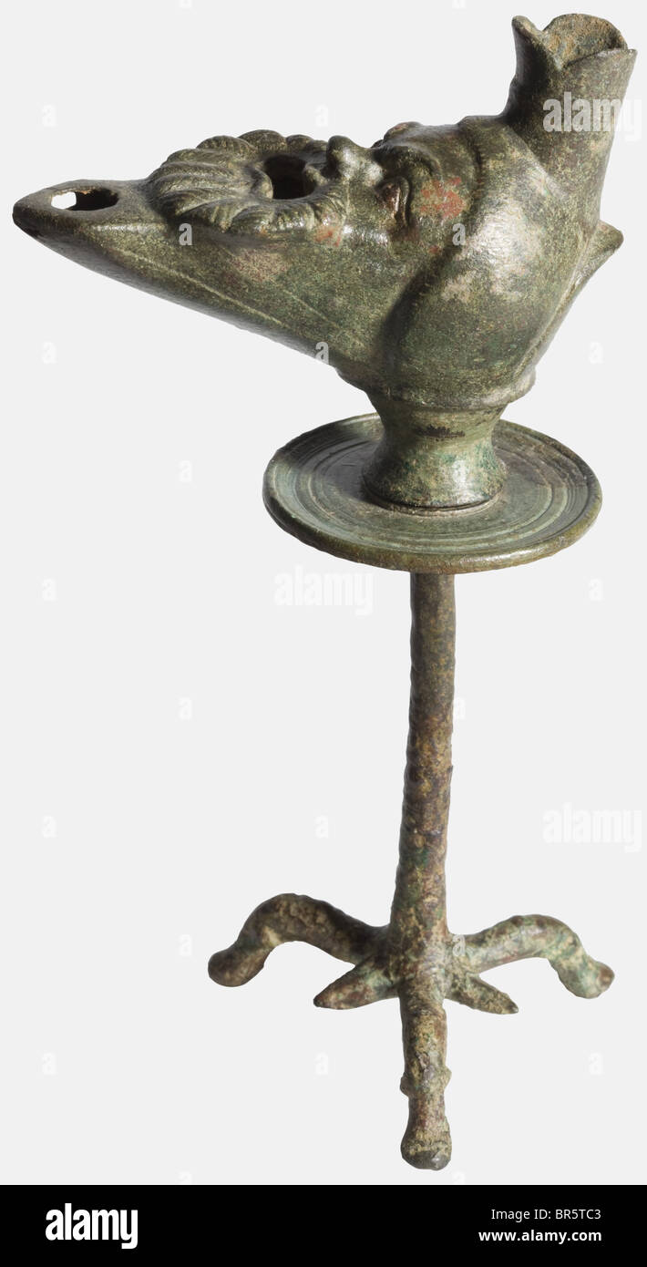 Une lampe en bronze romain avec trépied, bronze moulé 1ème/2ème siècle complété par le froid. En deux morceaux. La lampe en forme de masque de comédien barbu, la bouche - qui était remplie d'huile - yeux larges et expressifs, les bruns et le nez distinctement façonnés. Inclut un trépied se terminant par trois pieds d'animaux stylisés et évasés avec montage précis. Finement ciselé. Hauteur 16,8 cm. Patine légèrement repérée, petite écaille à l'avant du trou de mèche, petite réparation à la tige. Peter La Baume, Römisches Kunstgewerbe, 1983, Banque D'Images