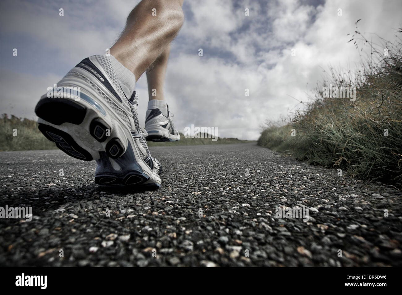 Un proche, low angle view of a male athlete running le long d'une route goudronnée avec ses grandes jambes montrant Banque D'Images