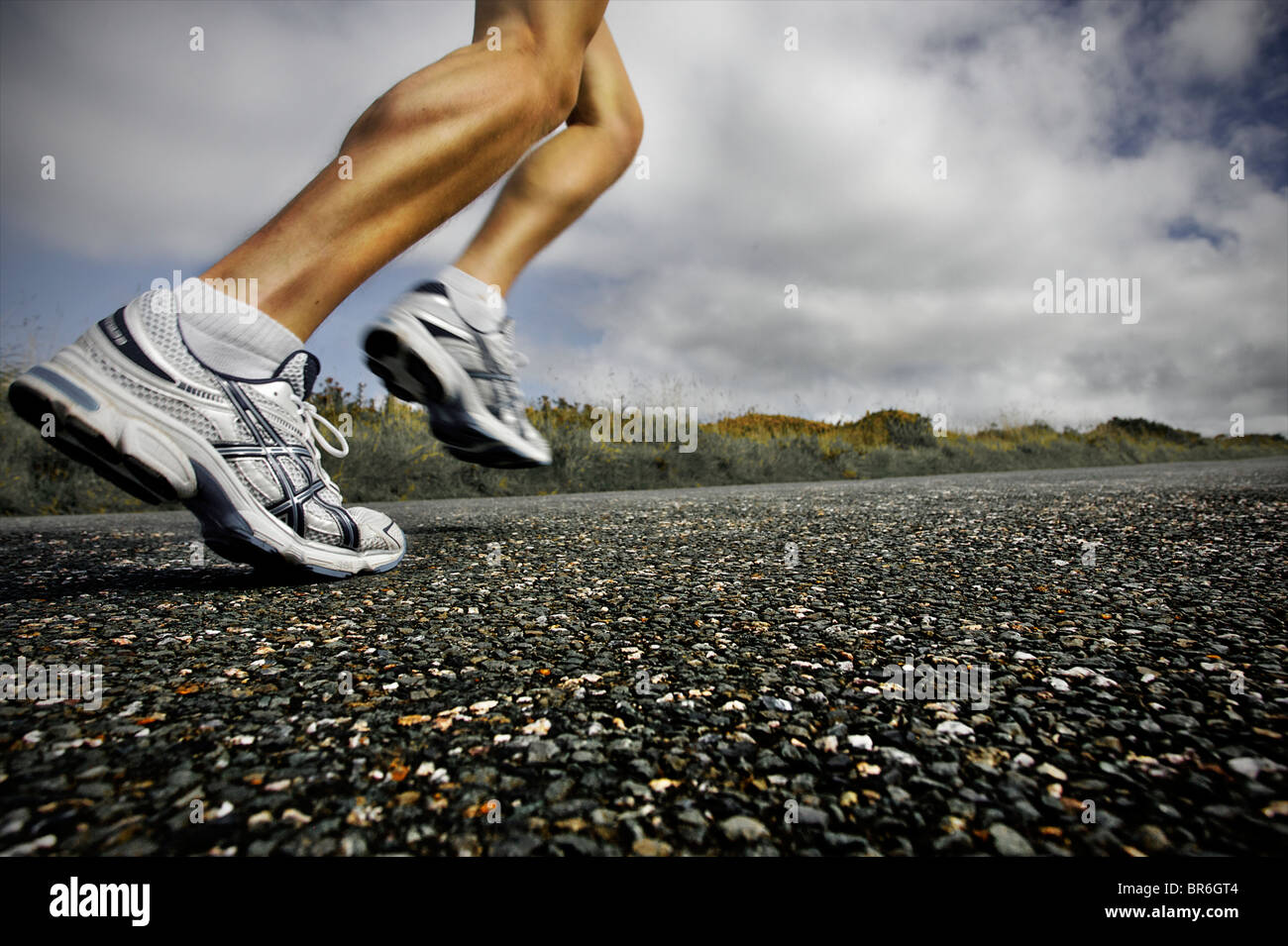 Un proche, low angle view of a male athlete running le long d'une route goudronnée avec ses grandes jambes montrant Banque D'Images