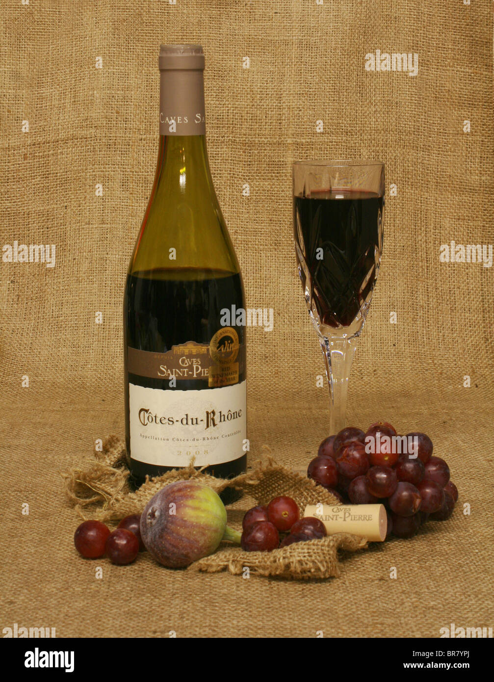 Bouteille de vin rouge et de vin dans un verre, avec des fruits sur un fond de toile. Banque D'Images