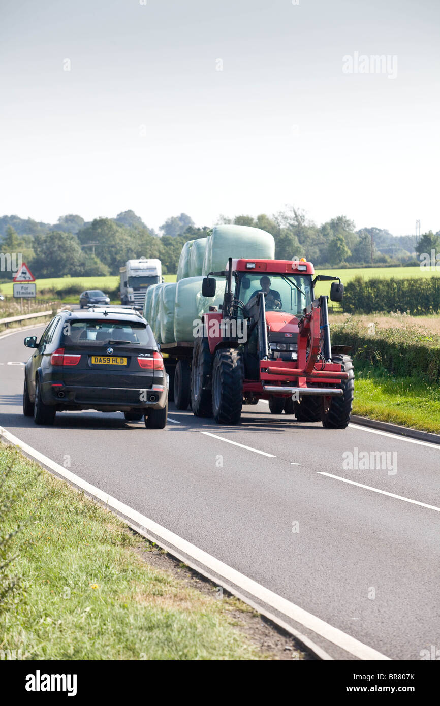 Tracteur agricole avec la circulation derrière elle sur une route rurale Banque D'Images
