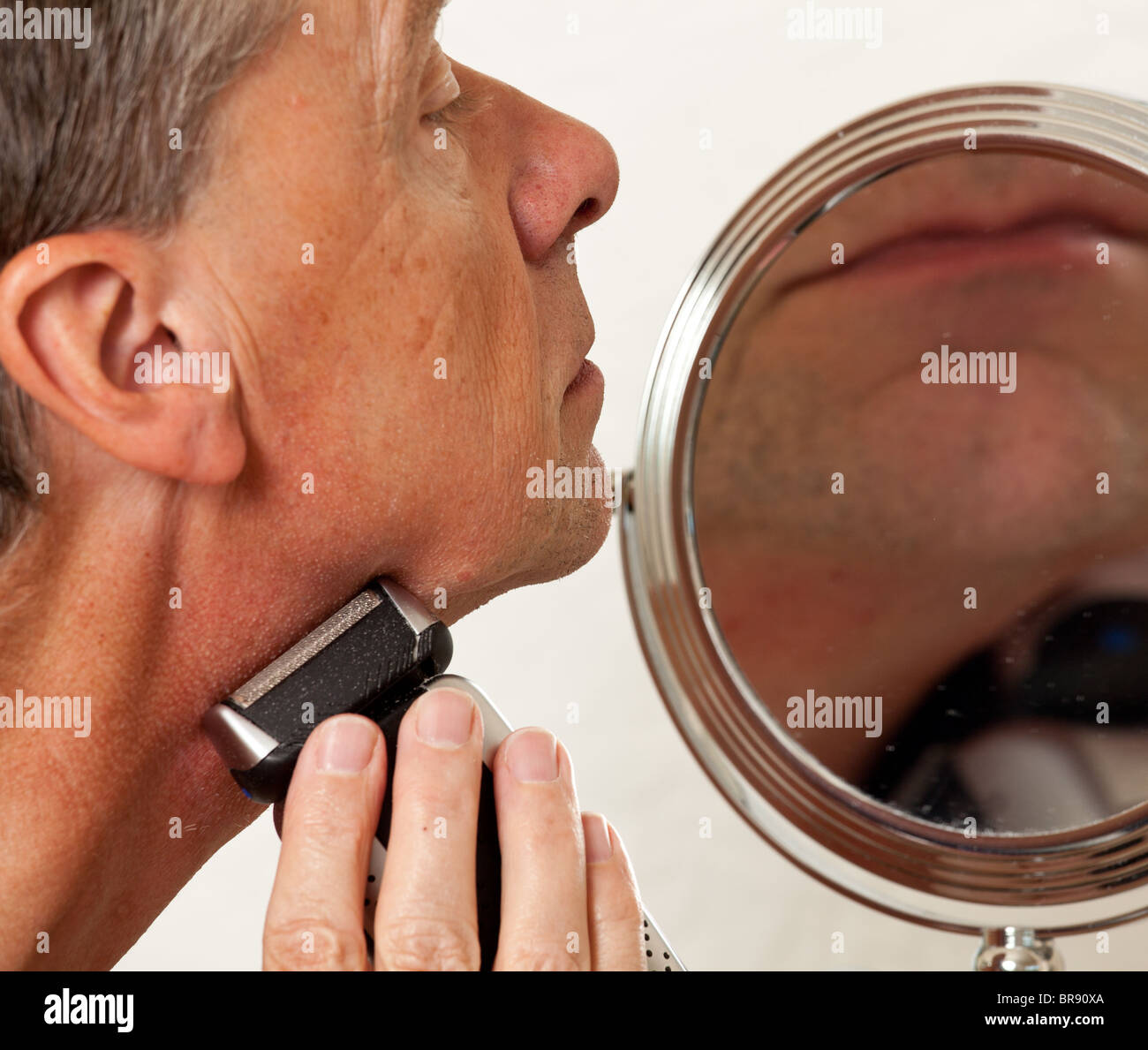 Homme d'âge moyen avec de rasage rasoir électrique en face de petit miroir Banque D'Images