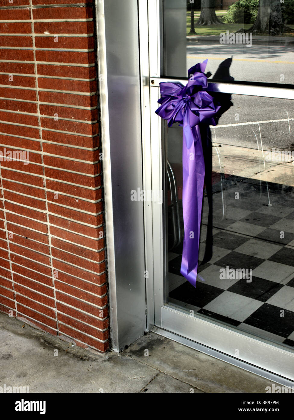 Grand arc violet et ruban accroché sur une porte de verre et d'argent dans un mur de brique avec plancher à carreaux réflexions visibles Banque D'Images