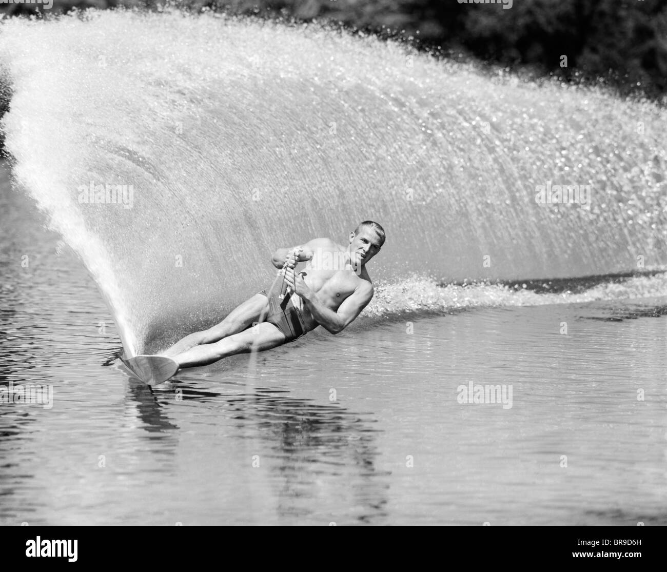 1970 slalom homme se penchant sur le côté pour créer mur d'eau de derrière Banque D'Images