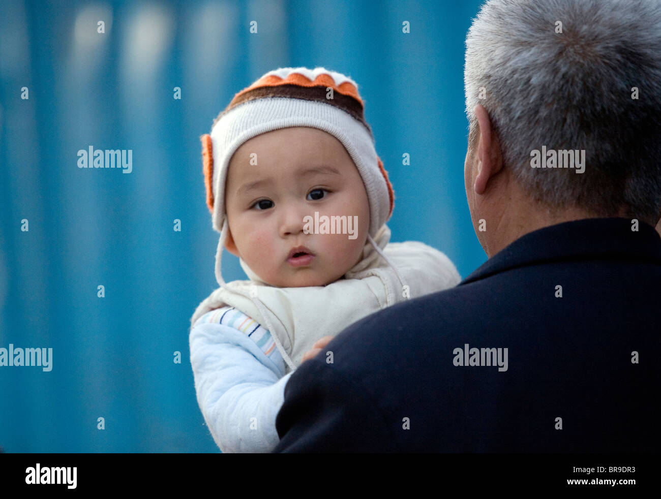 Un bébé donne de plus de l'épaule de son grand-père comme ils marchent ensemble dans une rue de Beijing en Chine. Banque D'Images