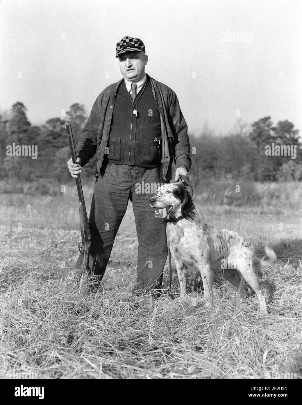 1930 MAN STANDING IN FIELD HOLDING SHOTGUN ET UNE LAISSE DE CHIEN SETTER GORDON Banque D'Images