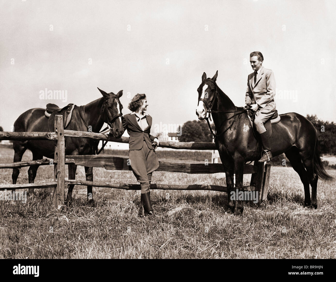 Années 1930 Années 1940 Équipement d'ÉQUITATION EN COUPLE MAN RIDING HORSE WOMAN STANDING BY CLÔTURE EN BOIS Banque D'Images