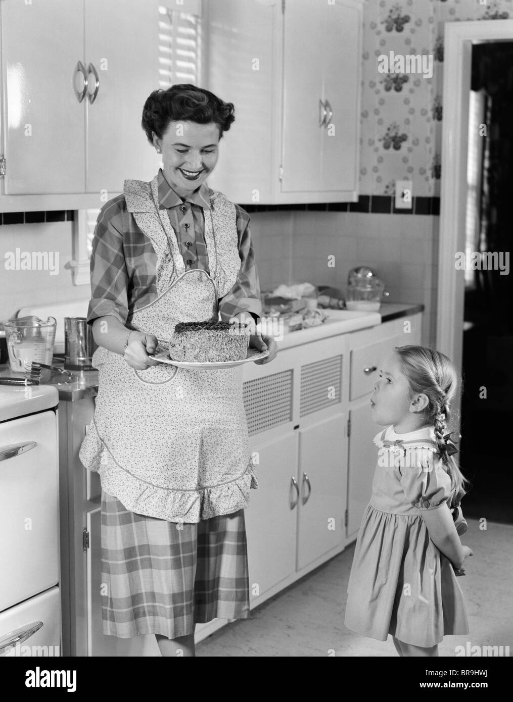 1950 Mère en montrant un gâteau à la fille de cuisine équipée Banque D'Images