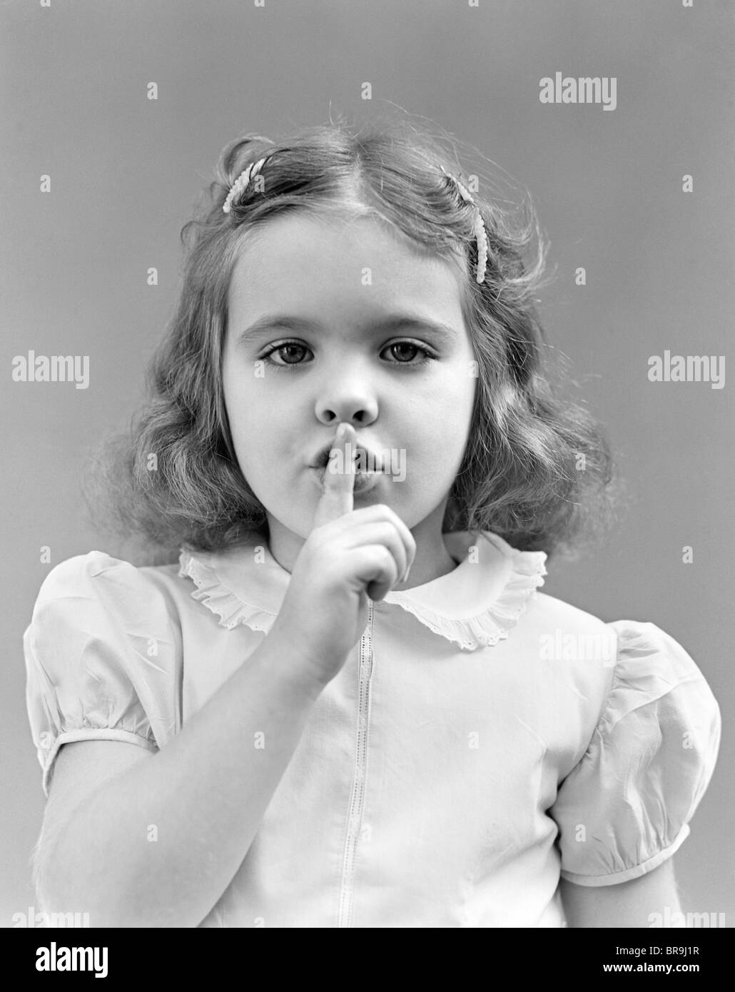Années 1940 Années 1950 GIRL AVEC LES DOIGTS POUR FAIRE DE GESTE CHUT CALME LÈVRES LOOKING AT CAMERA Banque D'Images