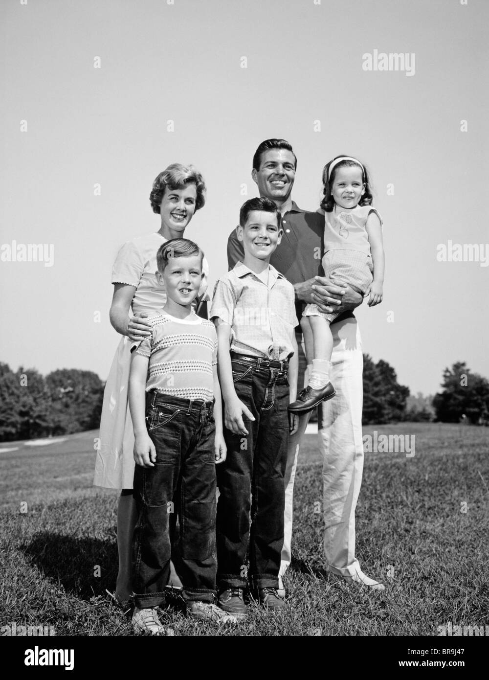 1960 SMILING FAMILY PORTRAIT DEBOUT SUR L'HERBE Mère Père TROIS ENFANTS Banque D'Images