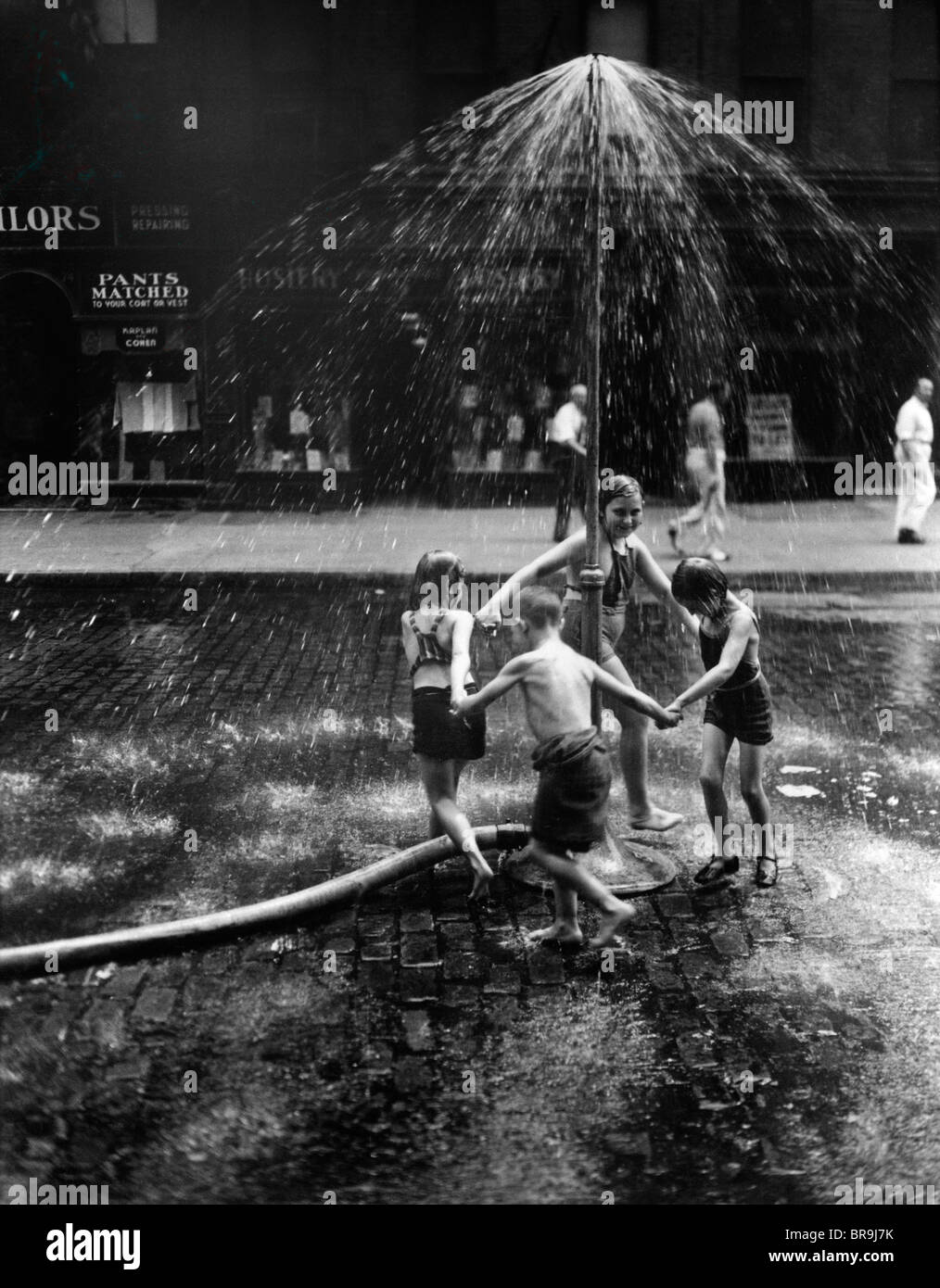 1930 ENFANTS JOUANT DANS LE CENTRE-VILLE DE PULVÉRISATION D'EAU D'INCENDIE WATER SPRINKLER Banque D'Images