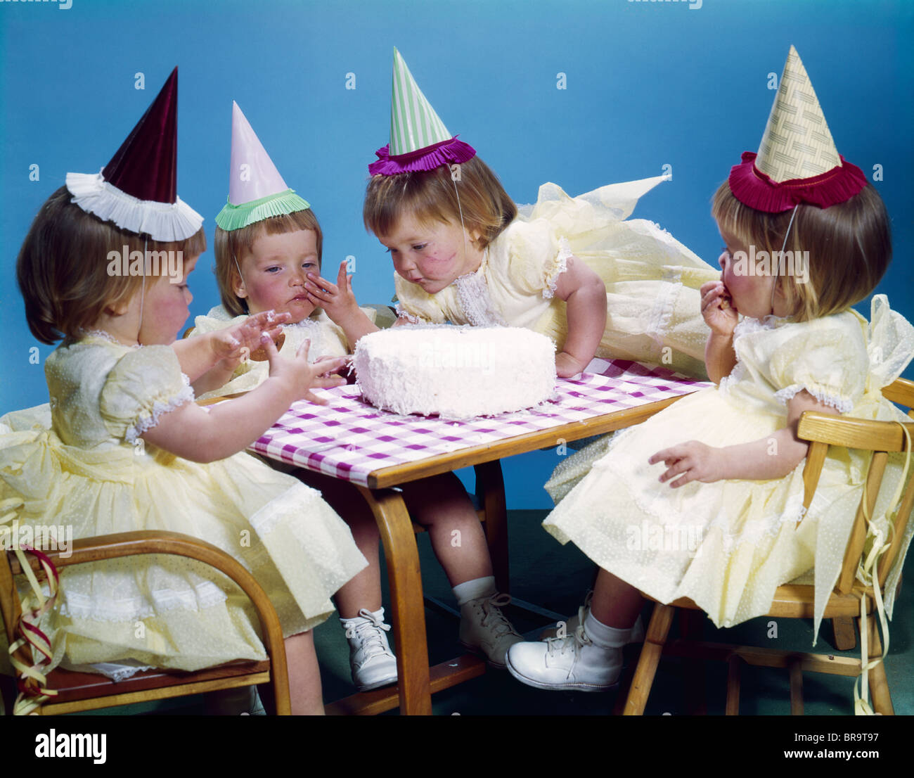 Années 1950 Années 1960 QUADRUPLÉS 4 Filles aux cheveux rouges WEARING PARTY HATS ET gâteau d'ANNIVERSAIRE DE LA TABLE DE SÉANCE ROBES Banque D'Images