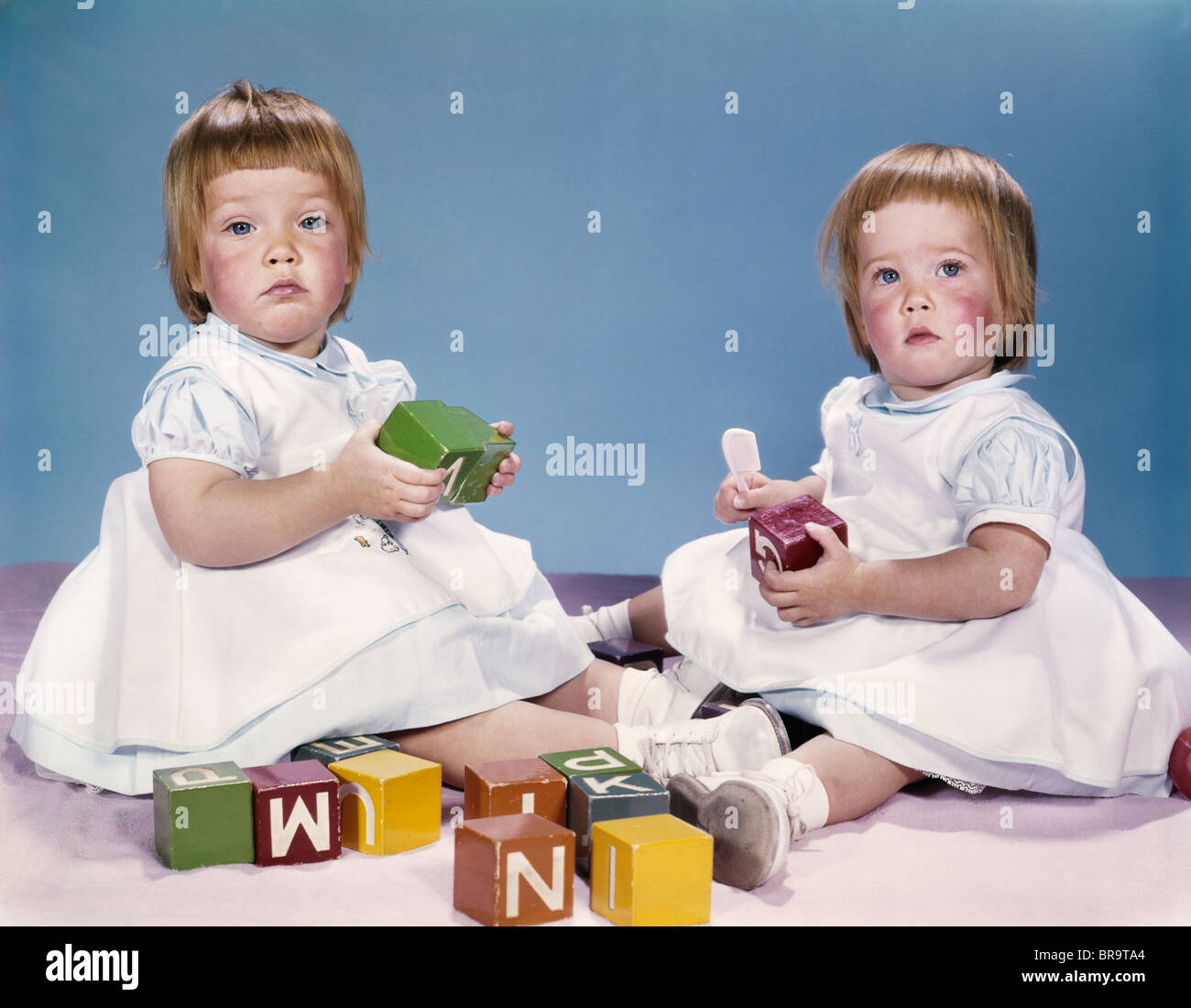 Années 1950 Années 1960 Portrait de deux lits bébé filles portant des robes PLAYING WITH TOY BLOCKS Banque D'Images