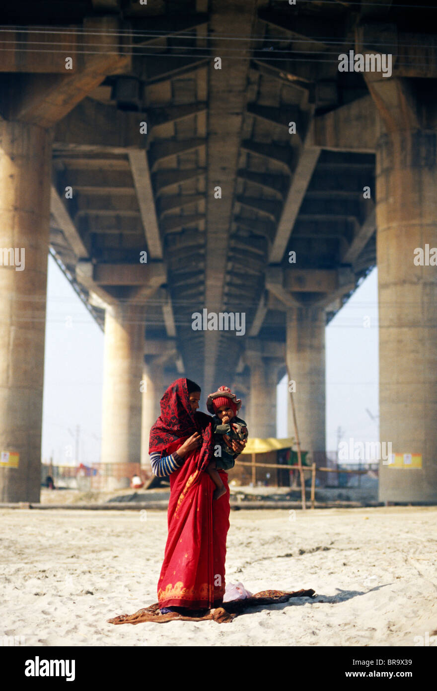Mère vêtue d'un sari rouge avec un enfant dans ses bras sous un pont à Allahabad en Inde. Banque D'Images