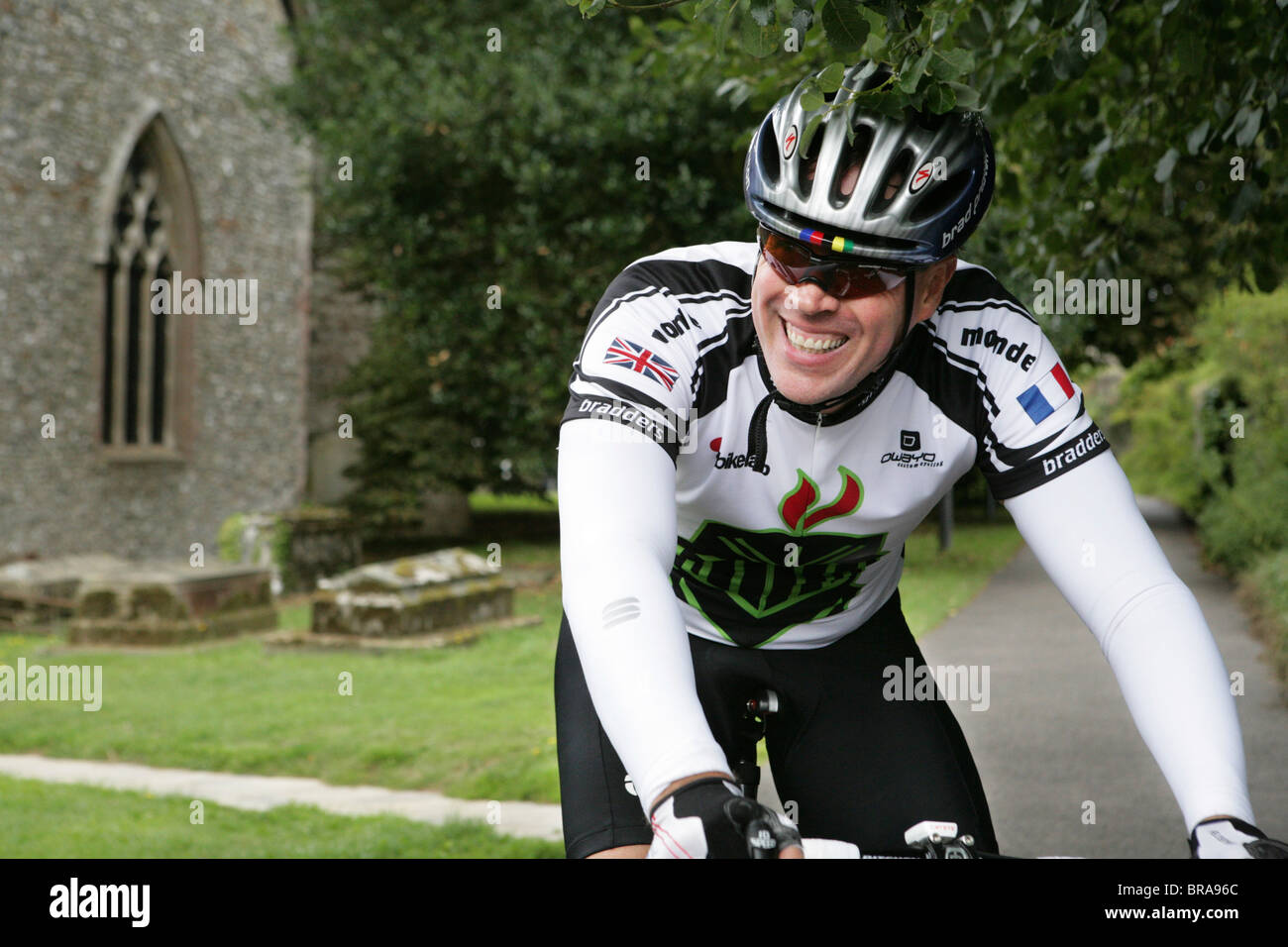 Un homme en tenue de vélo complet équitation sa moto à travers une cour de  l'église en Angleterre en souriant Photo Stock - Alamy