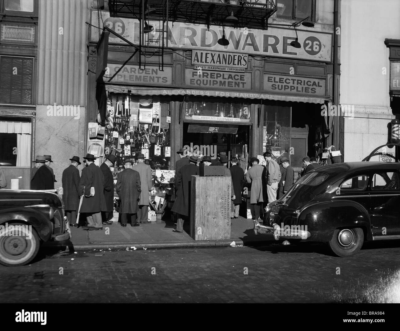 1940 NEW YORK CITY GROUPE FOULE TROTTOIR HOMMES PERSONNES SEULES EN FACE DE ALEXANDER'S HARDWARE STORE Banque D'Images