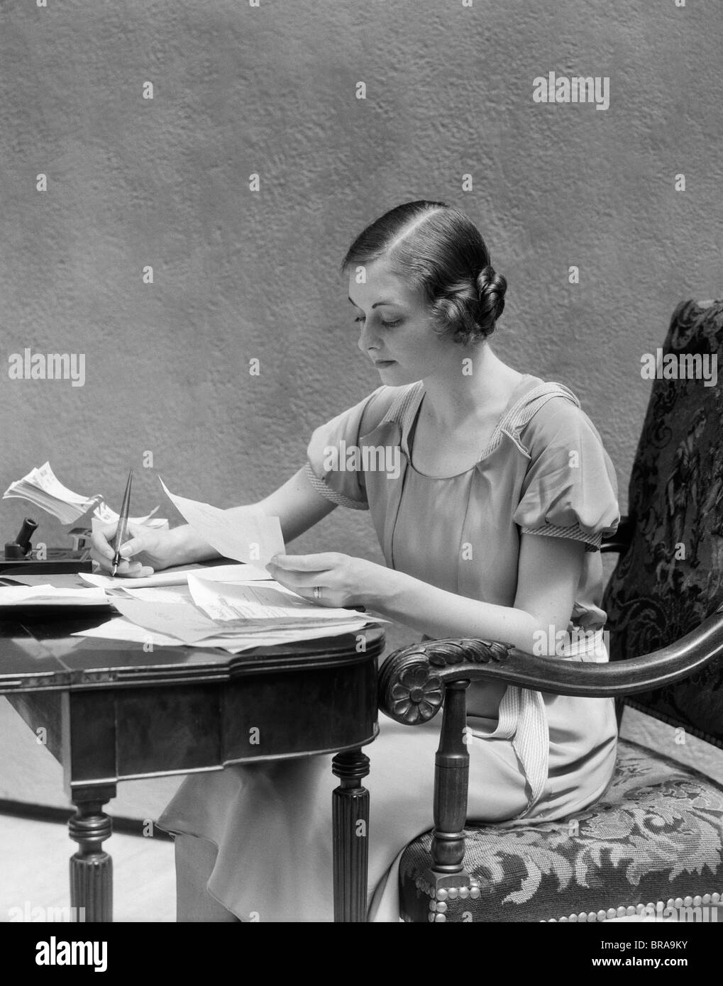 1930 WOMAN SITTING AT DESK TYPING LE PAIEMENT DES FACTURES l'écriture avec stylo Banque D'Images