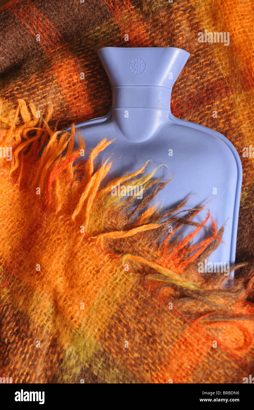Une bouteille d'eau chaude bleu partiellement couvert par une couverture de laine rouge à carreaux avec des franges. Banque D'Images