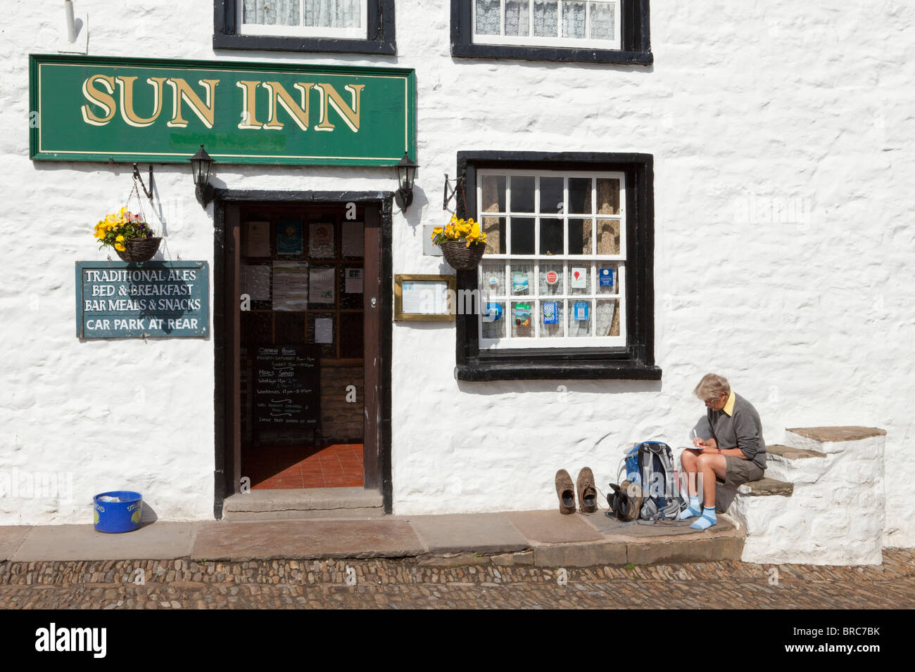 Une femme écrit randonneur cartes postales sur l'ancien bloc de montage à l'extérieur de l'auberge de soleil dans le village de Dent, Dentdale, Cumbria Banque D'Images