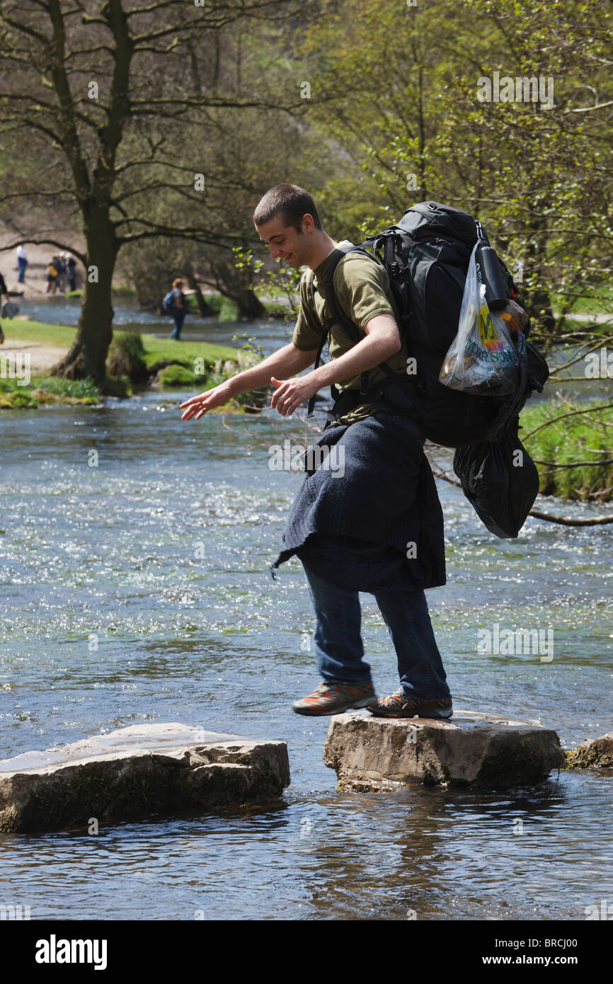 Walker avec sac à dos lourd traversant le Dovedale Stepping Stones, Peak District, Derbyshire Banque D'Images