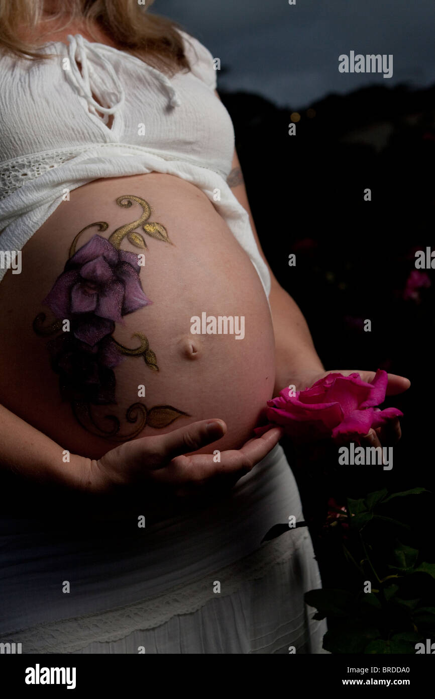 Shoot avec la maternité pregnant woman's belly peint par un artiste de maquillage, brandissait une rose rose près de son estomac Banque D'Images