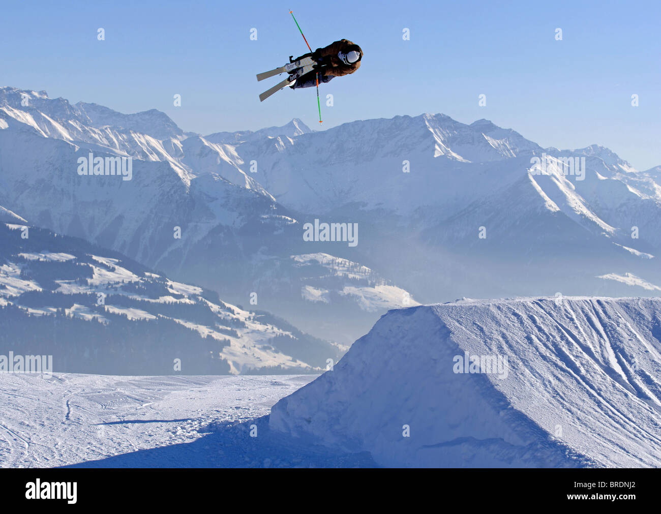 Un homme saute d'un skieur kicker dans un parc de neige tout en attrapant ses deux skis et spinning Banque D'Images