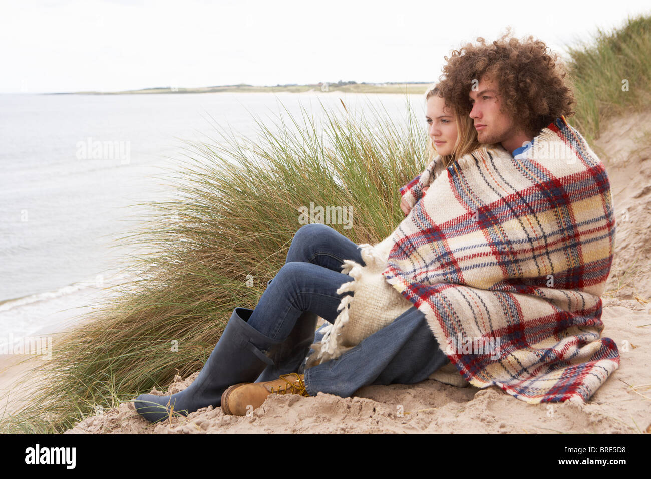 Teenage Couple Sitting in Sand Dunes enveloppé dans le contrat cadre Banque D'Images