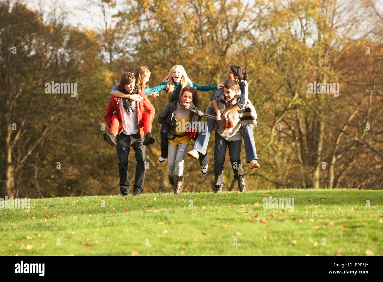 Groupe d'amis adolescents ayant Piggyback Rides en paysage d'automne Banque D'Images