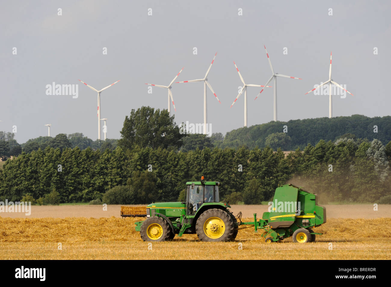 Allemagne tracteur John Deere et presse à balle à la récolte de paille et les éoliennes à l'horizon Banque D'Images