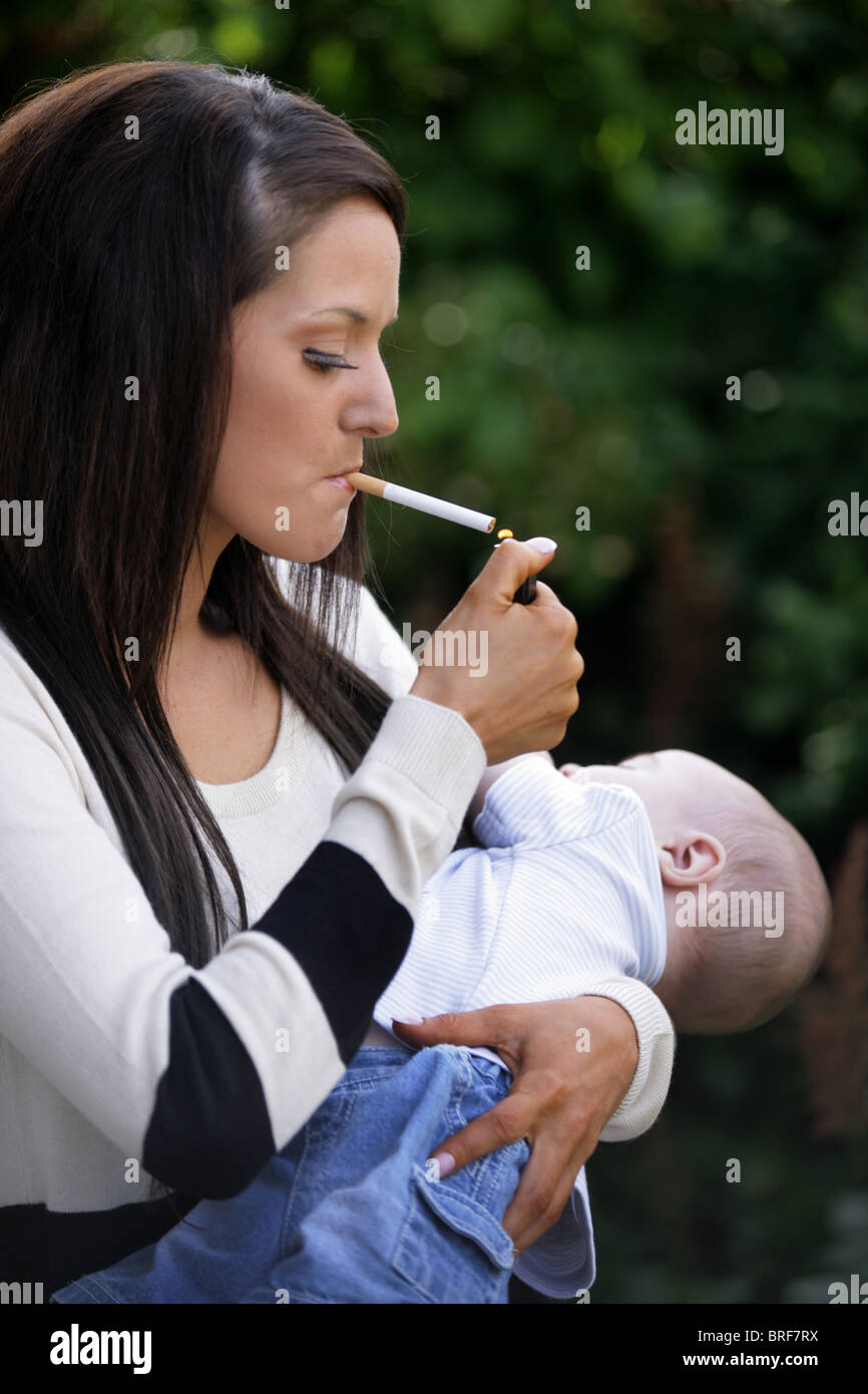 Mere Dans Sa Vingtaine De Fumer Une Cigarette Et Tenant Son Bebe Dans Les Bras Photo Stock Alamy