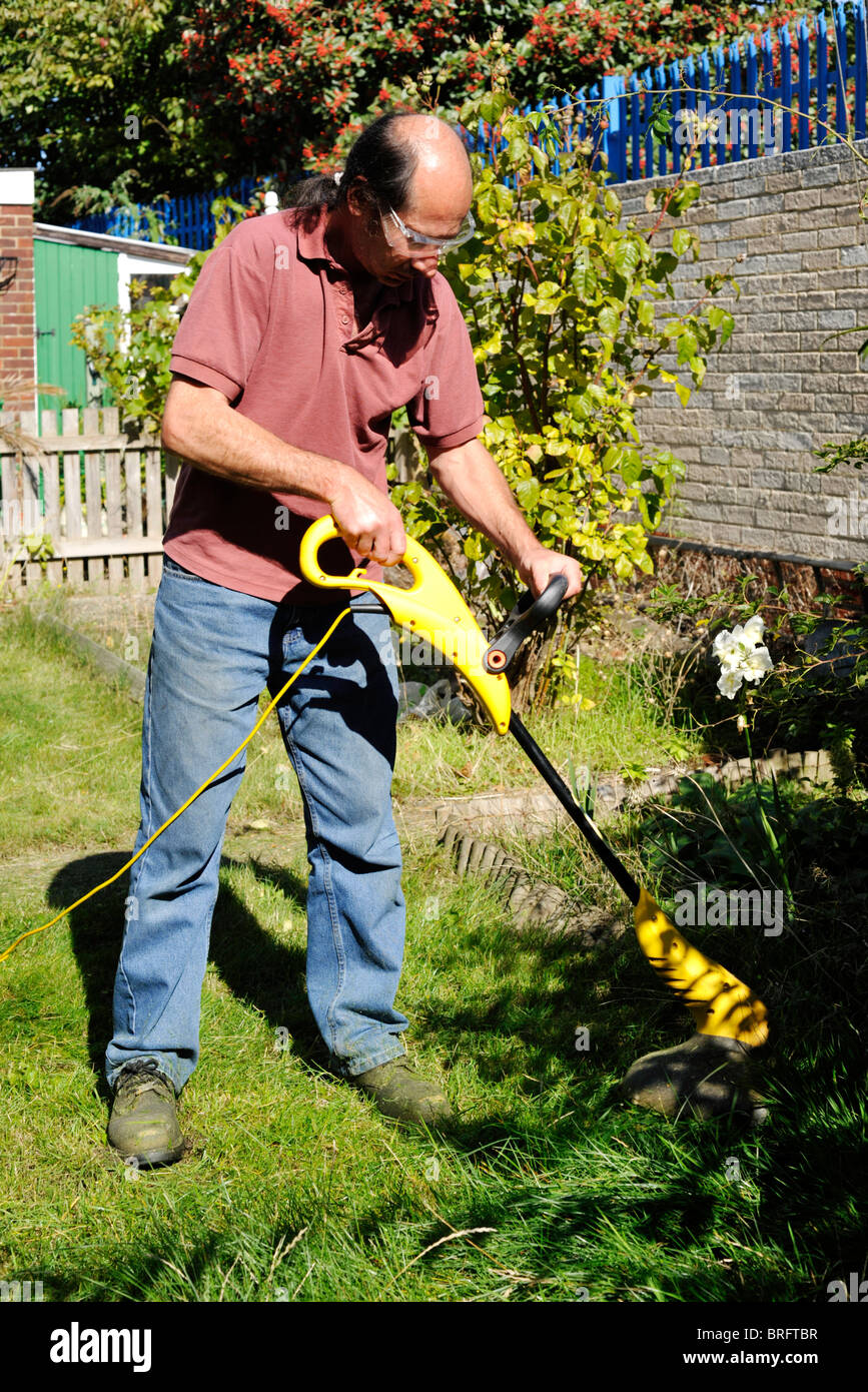 L'homme à l'aide d'un outil de coupe de gazon électrique pour couper l'herbe  dans son jardin Photo Stock - Alamy