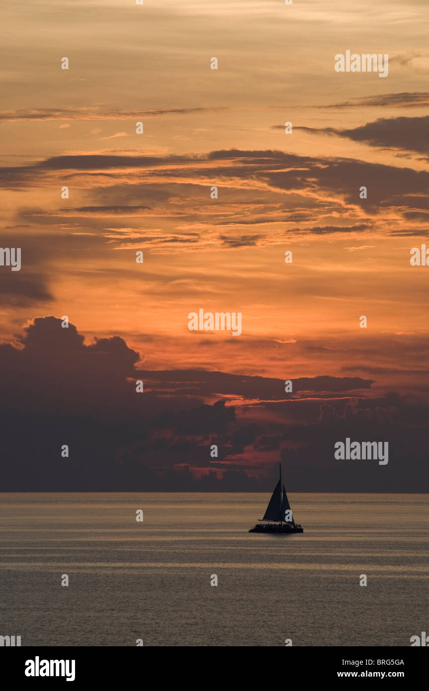 Un voilier navigue au large de Aruba avec un beau coucher de soleil en toile de fond. Banque D'Images