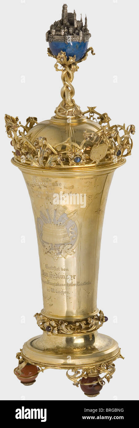 Une coupe trophée, pour le XVème Concours National de tir allemand, Munich 1906 UNE grande, en forme de calice, doré, tasse avec un couvercle.le couvercle porte une boule lapis-lazuli soutenue par des racines avec une miniature argentée de la ville de Munich.le bord est entouré de vigne contenant des boucliers avec des symboles de tir et des fleurs ensemble Sapphires, carnéliens et agates. Le côté opposé de la tasse affiche des outils de brassage entre les initiales 'J' et 'S' et les inscriptions 'Ehrengabe für das XV.Deutsche Bundesschießen München 1906'(Prix pour le XVème Allemand, droits additionnels-Clearences-non disponible Banque D'Images