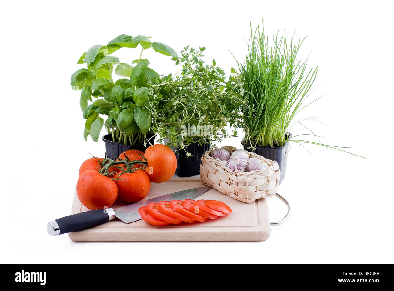 Des pots de basilic, thym et ciboulette avec des tranches de tomate, bouquet de tomates et l'ail dans le panier Banque D'Images