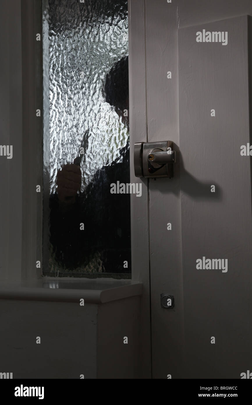 La figure d'une personne à l'extérieur à la recherche par le biais d'une fenêtre en verre opaque, tenant un couteau Banque D'Images