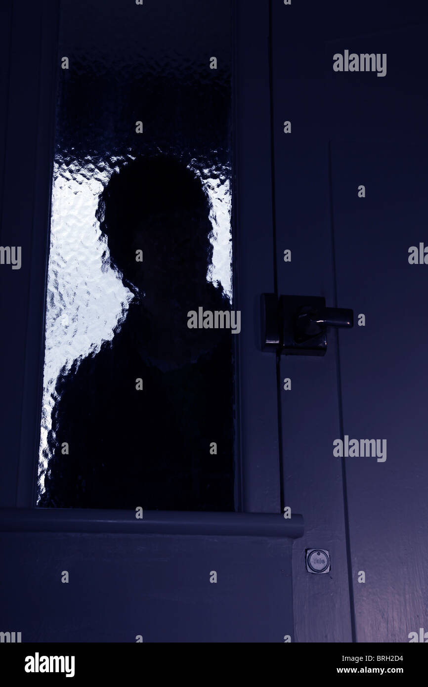 Silhouette homme intrus regardant à travers une fenêtre opaque à côté d'une porte d'entrée Banque D'Images
