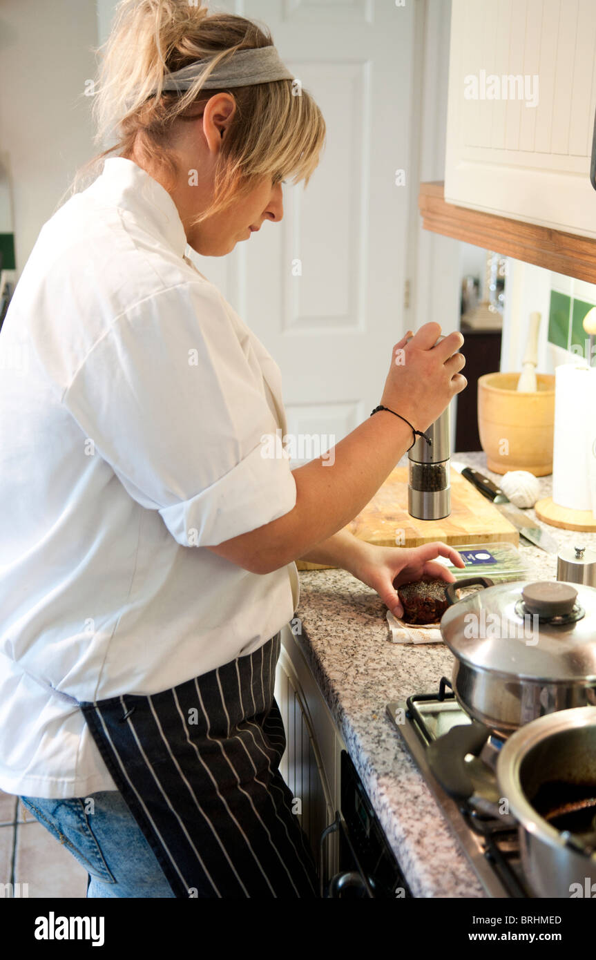 Femme chef steak assaisonnement avec du poivre dans la cuisine Banque D'Images